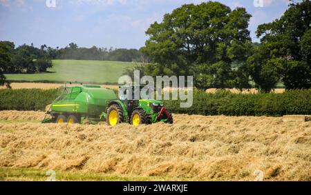 Tracteur John Deere 6155R avec une presse à balles L1534 dans la campagne du Wiltshire par une journée d'été ensoleillée. Banque D'Images