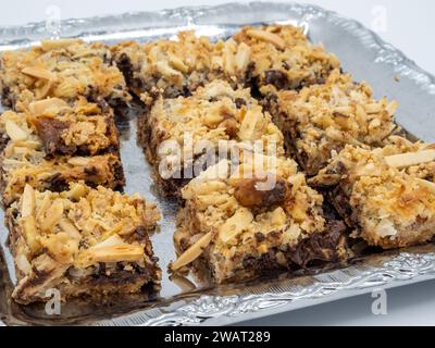 Une succulente sélection de brownies garnies de flocons d'amandes dorées, prêts à fondre dans votre bouche. Présenté sur plaque métallique isolé sur fond blanc. Banque D'Images