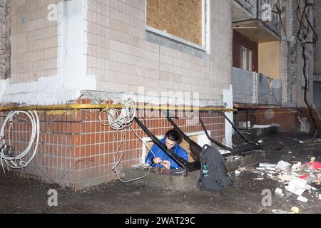 Un jeune homme est vu réparer une ligne Internet près d'une maison détruite. Un immeuble résidentiel de plusieurs étages dans le quartier Solomenskiy de la capitale a subi des dommages à la suite d'une frappe massive de missiles russes sur Kiev le 2 janvier. Le bâtiment a subi les pires dommages parmi les autres bâtiments résidentiels. Et de nombreux résidents ont été blessés et hospitalisés. Les sauveteurs et les bénévoles aident à enlever les déchets et les restes du bâtiment endommagé. Banque D'Images