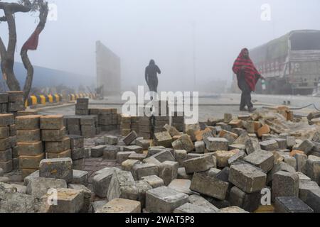 Les ouvriers marchent devant des pavés posés sur un trottoir nouvellement construit un matin brumeux avant la visite du Premier ministre indien Narendra Modi à Ayodhya. Ramnagari Ayodhya, autrefois connu pour ses rues étroites et ses routes en décomposition, progresse régulièrement : toutes les routes et bâtiments menant à RAM Janmabhoomi sont en cours d’élargissement et de rénovation pour faciliter les déplacements. Banque D'Images