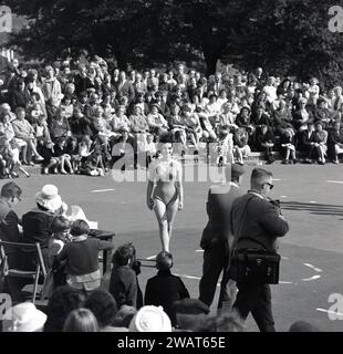 Années 1960, historique, une foule de spectateurs regardant un concours de reine de beauté, avec une jeune femme en maillot de bain valant devant les juges et les photographes en exercice, Angleterre, Royaume-Uni. Dans la Grande-Bretagne d'après-guerre, des concours de beauté ont été organisés tout au long de l'été dans les stations balnéaires pour offrir des divertissements aux personnes en vacances. En 1945, Morecambe dans le Lancashire voit le premier concours Miss Grande-Bretagne avoir lieu. Banque D'Images