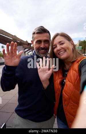 Couple caucasien mature souriant prenant un selfie vertical à l'extérieur en utilisant un téléphone portable. Banque D'Images