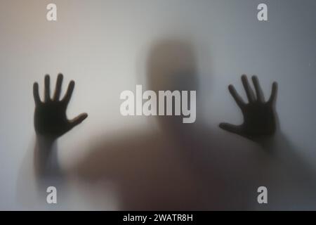 Homme avec la silhouette des mains levées derrière le verre dépoli Banque D'Images