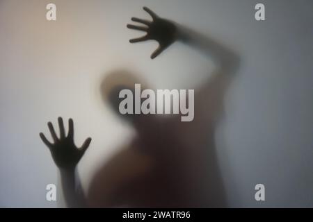 Homme avec la silhouette des mains levées derrière le verre dépoli Banque D'Images