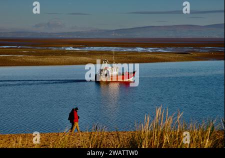 Une promenade le long de la plage au crépuscule, alors qu'un chalutier de pêche rentre au port, Fleetwood, Lancashire, Royaume-Uni, Europe samedi, 5 janvier 2024 Banque D'Images