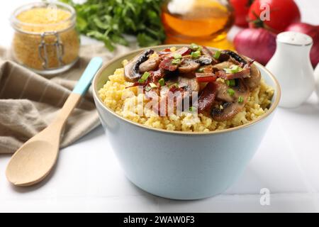 Savoureux porridge de millet avec des champignons, du bacon et de l'oignon vert dans un bol sur une table blanche, gros plan Banque D'Images