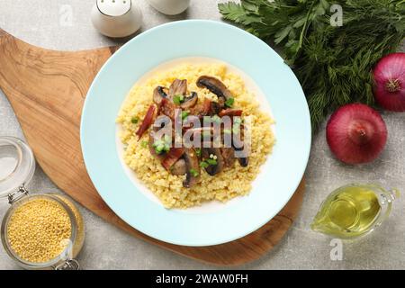 Savoureuse bouillie de millet avec champignons, bacon et oignon vert sur table texturée grise, mise à plat Banque D'Images