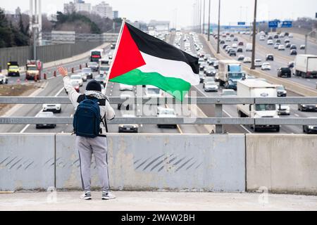 Un manifestant anti-israélien agite un drapeau palestinien aux conducteurs sur l'autoroute 401 alors qu'ils passent sous le pont supérieur Avenue Road à Toronto. Banque D'Images