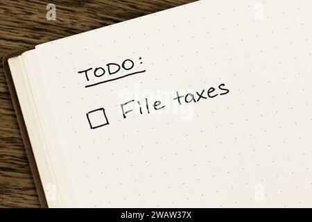 Liste des tâches avec rappel à cocher « taxes sur les fichiers » écrit à la main sur un carnet à grille à points ouverts sur un bureau en bois texturé, à plat, vue de dessus Banque D'Images