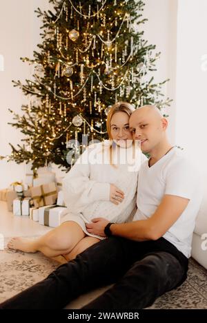 Couple semble très heureux. Un beau mari embrasse sa belle femme enceinte à côté de la fenêtre du salon. Banque D'Images