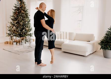 Couple semble très heureux. Un beau mari embrasse sa belle femme enceinte à côté de la fenêtre du salon. Banque D'Images