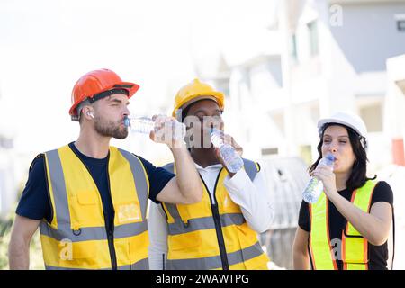 Équipe d'ingénieurs de travailleurs en bonne santé assoiffée buvant de l'eau propre dans la température chaude saison d'été pour se détendre frais sur le lieu de travail du chantier de construction. Banque D'Images