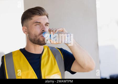 Équipe d'ingénieurs de travailleurs en bonne santé assoiffée buvant de l'eau propre dans la température chaude saison d'été pour se détendre frais sur le lieu de travail du chantier de construction. Banque D'Images