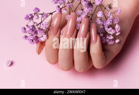 Les mains féminines avec un design de clou rose tiennent des fleurs de gypsophila. Manucure de vernis à ongles rose sur fond rose Banque D'Images