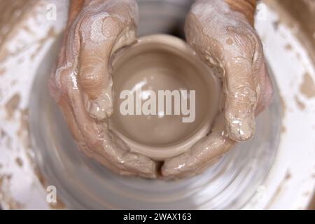 Mains masculines faisant tasse en céramique sur la roue de poterie, gros plan, vue de dessus. homme faisant tasse à partir d'un pot d'argile Banque D'Images