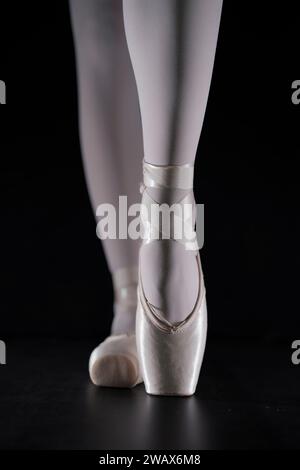 détail des pieds de danseuse de ballet en position de ballet avec la chaussure de pointe devant le fond sombre Banque D'Images