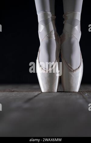 détail des pieds de danseuse de ballet en position de ballet avec la chaussure de pointe devant le fond sombre Banque D'Images