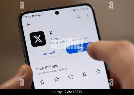 Un doigt pointant vers la page d'installation de l'application X (anciennement twitter) sur un écran de smartphone par la société américaine X Corp, Royaume-Uni Banque D'Images
