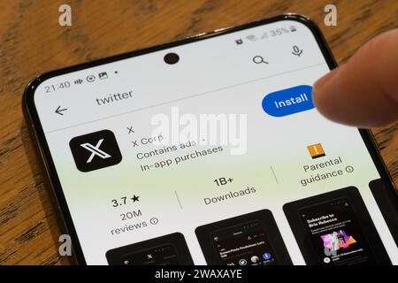 Un doigt pointant vers la page d'installation de l'application X (anciennement twitter) sur un écran de smartphone par la société américaine X Corp, Royaume-Uni Banque D'Images