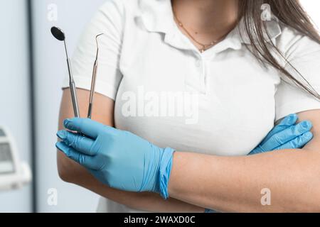 Un dentiste tenant des instruments dentaires dans sa main, qui sait comment créer de beaux sourires, posant dans son cabinet dentaire, transmettant confiance et Banque D'Images