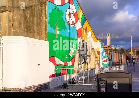 Southampton, Royaume-Uni. 6 janvier 2024.un artiste peint une fresque colorée et vibrante sur le mur des escaliers du côté sud de la gare centrale de Southampton, dans le cadre du récent projet de réaménagement de la gare centrale de Southampton. Ce projet a été financé par le Fonds pour la transformation des villes du gouvernement et soutenu par Network Rail et South Western Railway . L'œuvre présente les points forts de la ville de Southampton.le design a été créé par l'artiste local Poppy Ash. Banque D'Images