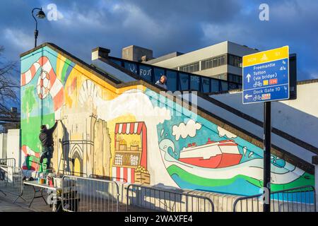 Southampton, Royaume-Uni. 6 janvier 2024.un artiste peint une fresque colorée et vibrante sur le mur des escaliers du côté sud de la gare centrale de Southampton, dans le cadre du récent projet de réaménagement de la gare centrale de Southampton. Ce projet a été financé par le Fonds pour la transformation des villes du gouvernement et soutenu par Network Rail et South Western Railway . L'œuvre présente les points forts de la ville de Southampton.le design a été créé par l'artiste local Poppy Ash. Banque D'Images