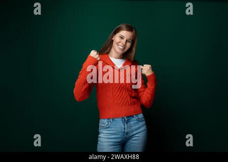 Jolie jeune femme vêtue d'un pull rouge souriant sur un fond vert Banque D'Images