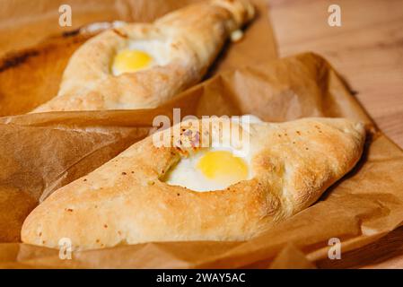 Deux morceaux de Khachapuri géorgien traditionnel, un pain fourré de fromage avec un œuf au soleil cuit au centre, sur papier parchemin. Banque D'Images