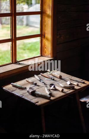 Un ensemble d'outils de sculpture sur bois anciens sur une table en bois près de la fenêtre. Le métier de fabriquer des sabots. Banque D'Images