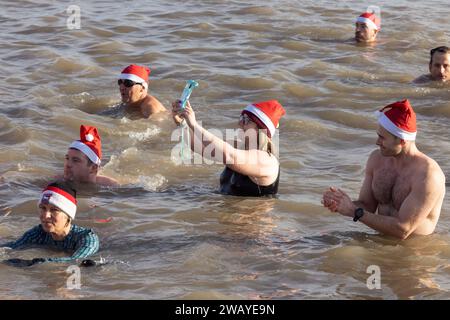 Femme prend un selfie alors qu'elle est dans la mer avec d'autres nageurs à la nage de Boxing Day d'Aldeburgh. Aldeburgh, Suffolk. ROYAUME-UNI Banque D'Images