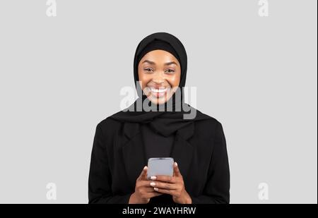 Heureuse jeune femme afro-américaine dans le hijab bavarder sur téléphone dans les réseaux sociaux Banque D'Images