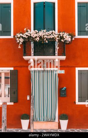 Une image architecturale d'un bâtiment de couleur orange avec deux petites fenêtres et des pots de fleurs sur le balcon, posé contre un ciel bleu clair Banque D'Images