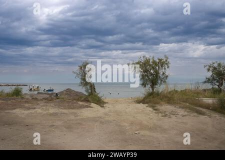 Nuageux jour de printemps pluvieux sur la plage au nord de l'île. Route sablonneuse avec quelques buissons et arbres. Eau calme. Montagnes en arrière-plan. Inten Banque D'Images