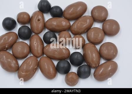 Chocolats de différentes tailles, arachides, noix, raisins secs sont recouverts de chocolat au lait et de glaçage au chocolat noir, cailloux disposés sur un fond blanc Banque D'Images