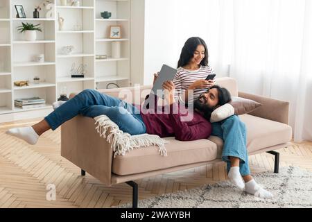 Joyeux homme et femme de l'est avec des gadgets refroidissant à la maison Banque D'Images