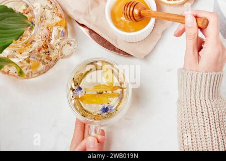 Les mains des femmes ajoutent du miel à la tasse de thé. Mode de vie sain de tisane de montagne. Concept d'herbes détoxifiantes Banque D'Images