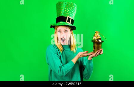 Femme blonde surprise en costume de Leprechaun avec pot d'or. Fête de la Saint Patrick. Traditions irlandaises. Pot avec de l'argent pour la journée de Patrick Banque D'Images