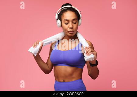 Femme de fitness afro-américaine portant un tracker et des écouteurs, fond rose Banque D'Images