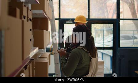 Superviseur afro-américain et stagiaire préparant les commandes d'entrepôt pour la livraison, utilisant la tablette pour vérifier les informations d'expédition, recevant un appel téléphonique tout en scannant les étiquettes de stock dans le centre de distribution Banque D'Images