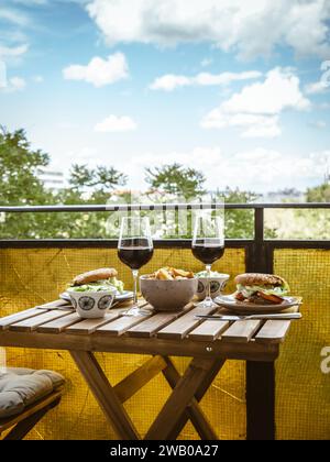 Table pour un dîner maison date de déjeuner sur un balcon avec hamburgers frites salade et vin, date romantique pour deux à la maison, nourriture maison Banque D'Images