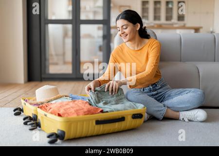 Souriant jeune femme indienne emballant joyeusement valise à la maison Banque D'Images