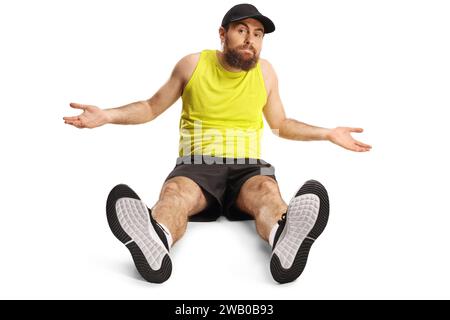 Homme barbu confus en vêtements de sport sur le sol et faisant des gestes avec des mains isolées sur fond blanc Banque D'Images