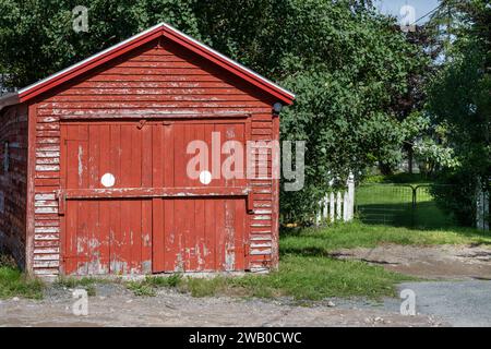 Un garage ou une grange en bois rouge vif vintage. Il y a deux portes en bois avec des taches blanches, toit en pointe et peinture écaillée. La structure de l'affleurement est ancienne. Banque D'Images