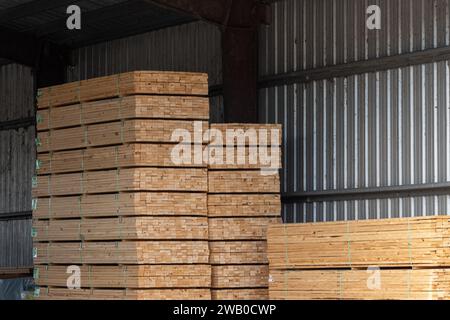 Planches de bois stockées dans une cour de bois. Les morceaux de bois de deux par quatre sont empilés haut dans un entrepôt métallique pour l'achat par le consommateur. La contrainte de construction Banque D'Images