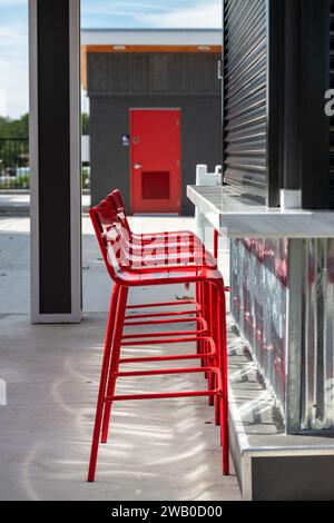 Trois chaises de bar en métal rouge vif sont devant un élégant comptoir en métal. Le haut de la barre est de couleur grise. Le mur moderne à motifs en aluminium est brillant Banque D'Images