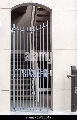 Le mur extérieur de couleur crème d'une résidence avec un portail en fer forgé à l'entrée de l'escalier. Sur la porte en métal ornée, le mot Private. Banque D'Images