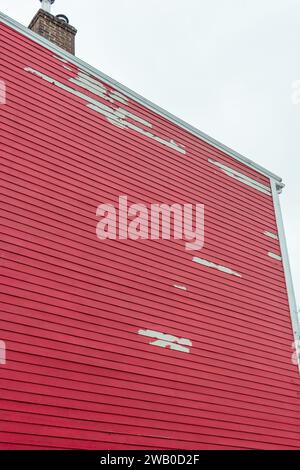 Le mur extérieur d'un bâtiment rouge vif. Le bois texturé est fait de feuillard de pin et la planche est horizontale sur la maison. La peinture se décolle. Banque D'Images