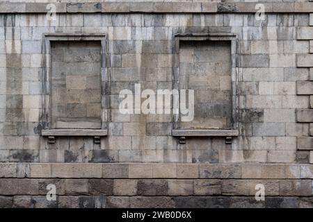 L'extérieur d'un vieux bâtiment en briques avec deux cadres de fenêtres scellés avec des blocs maçons gris et du béton. C'est un entrepôt altéré ou un mur d'usine. Banque D'Images