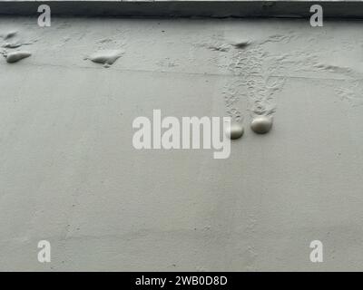 Un mur extérieur en ciment gris peint avec une texture. Des bulles ou des cloques d'humidité coulent le long du mur à cause des dégâts d'eau. Banque D'Images