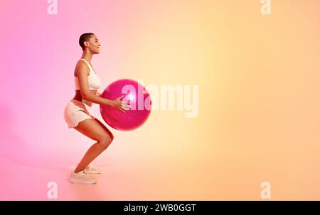 Une femme en forme avec une tête rasée effectue un exercice de squat avec une balle de fitness rose Banque D'Images